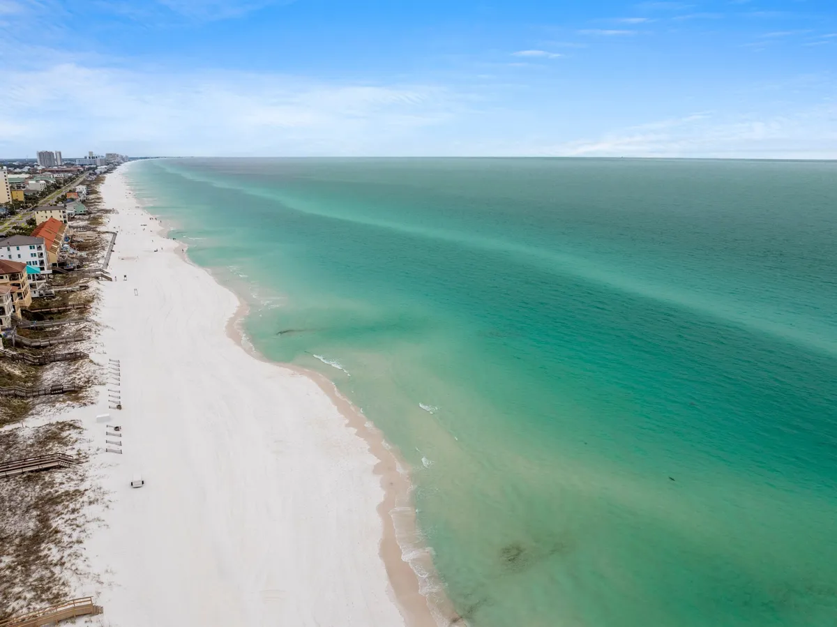 A wide-angle perspective of an expansive, uncrowded beach with turquoise water and some coastal buildings in the distance. The scene conveys a sense of openness and tranquility ideal for families to enjoy various beach activities.