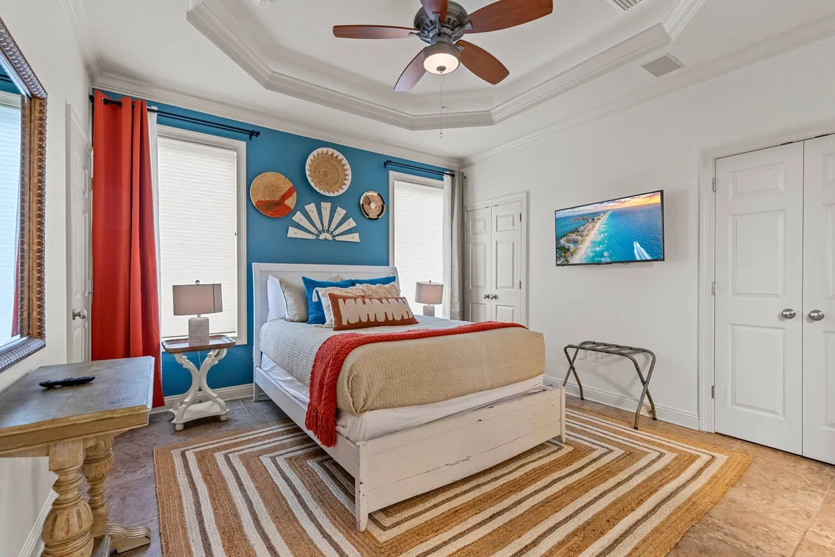 A cheerful guest bedroom with a bed accented by colorful throw pillows, a blue accent wall, decorative wall art, and a striped area rug. Natural light fills the room, creating a cozy and welcoming ambiance.