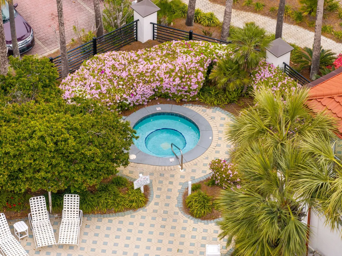 A circular hot tub with crystal-clear water, surrounded by lush greenery and pink flowering shrubs. White lounge chairs are arranged around the space for sunbathing or unwinding, creating a peaceful yet luxurious outdoor retreat.