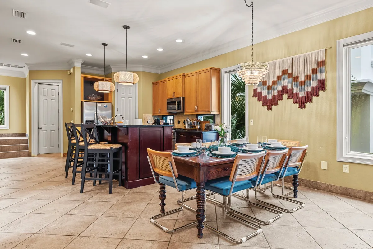 A modern dining area set for six, featuring a stylish table, kitchen island with bar stools, and contemporary cabinetry. Decorative touches and soft lighting foster a relaxed, welcoming environment perfect for shared meals and conversation.