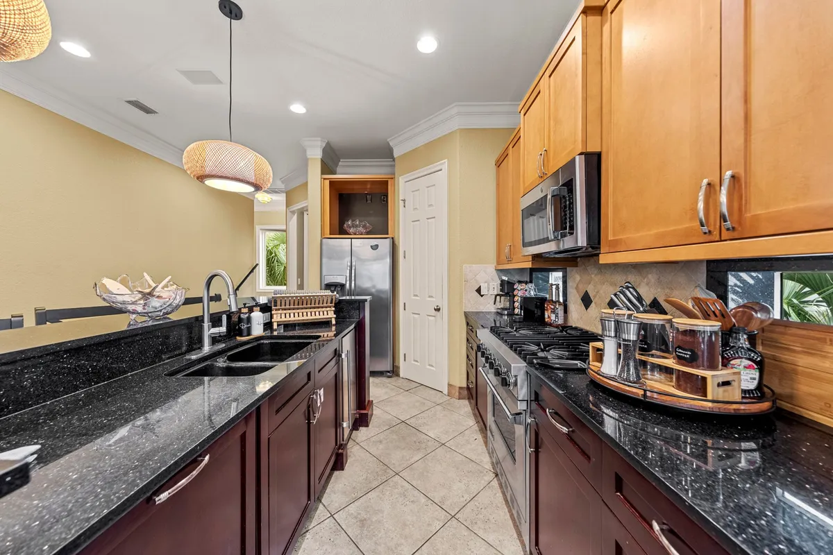 A close view of black granite countertops with a stainless steel refrigerator and microwave, complemented by dark wood cabinetry and modern pendant lighting above. The counter provides space for casual dining or meal prep, inviting family interaction.